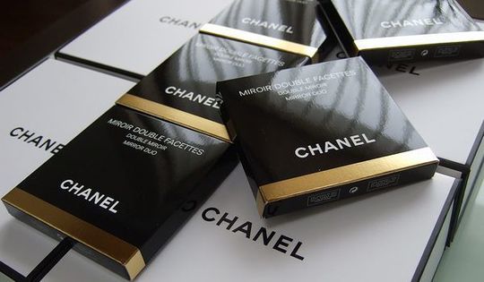 シャネルのコンパクトミラーが小さな箱に包まれ、美しく並べられたシンプルでエレガントな写真。特別なギフトとしての高級感が際立つシーン。