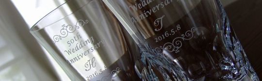バカラのベルーガハイボールペアグラスの側面に「50th Wedding Anniversary」の文字とそれぞれのイニシャル、記念日が名入れ彫刻され、装飾的なフレームで囲まれた美しいデザイン。50年の愛と絆を祝う特別な記念品