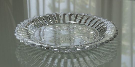 バカラのミルニュイプレートがテーブルの上に置いてある写真。繊細なプリーツ状のカットが施されたプレートが、光を反射して幻想的な輝きを放ち、食卓を華やかに彩る存在感を演出しています。名入れギフトとしても、特別な日を祝うテーブルウェアとしても最適な贈り物です。