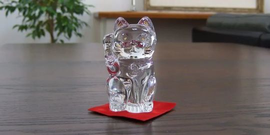 バカラの招き猫 クリアSサイズがテーブルの上に置いてある写真。透明なクリスタル製の招き猫が、その美しいフォルムと光の反射で、空間に幸運と洗練された雰囲気をもたらしています。名入れギフトとしても、インテリアとしても魅力的な逸品です。