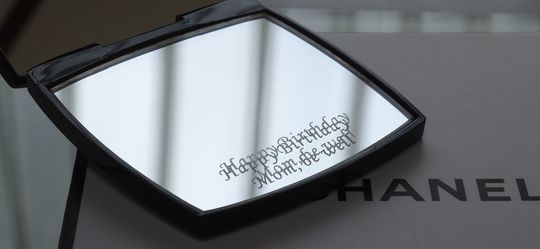 シャネルの名入れミラーに『Happy Birthday Mom, be well』というメッセージが刻まれた、母への感謝を伝える特別なギフト。洗練されたデザインで、感謝の気持ちを美しく表現。