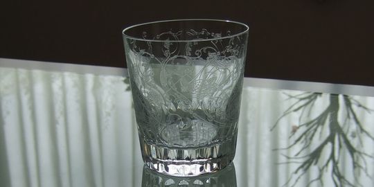 バカラのタンブラー（ロックグラス）の名入れページの商品一覧で使用する写真。バカラ パルメタンブラーがテーブルの上に置かれています。タンブラー全体にほどこされた繊細なエッチング装飾には、楽園に棲む空想の鳥と花々がモチーフとして描かれています。