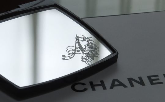 シャネルのコンパクトミラーの下部ミラーに、エレガントなバラの装飾とイニシャル『A』を名入れ彫刻した写真。華やかで繊細なデザインが高級感を醸し出す、特別なギフト仕様のイメージ。