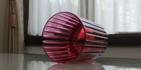 バカラグラスのハーモニータンブラー レッドがテーブルの上に置いてある写真。縦に施された繊細なカットが特徴のハーモニータンブラーのレッドクリスタルが、光を反射して鮮やかに輝いています。名入れギフトとしても、特別な日を彩るテーブルウェアとしても魅力的な逸品です。