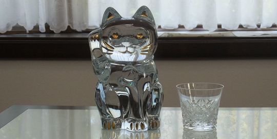 バカラの招き猫 クリアMサイズがテーブルの上に置いてある写真。透明なクリスタル製の招き猫が、その美しいフォルムと光の反射で、空間に幸運と洗練された雰囲気をもたらしています。名入れギフトとしても、インテリアとしても魅力的な逸品です。