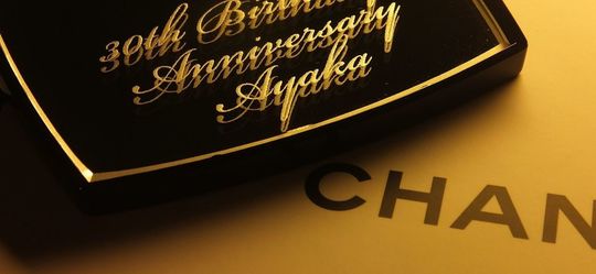 シャネルのミラー下部に、流麗なスクリプト体（筆記体）で『30th Birthday anniversary Ayuka』と名入れ彫刻を施した写真。30歳の節目を祝う特別なメッセージとお名前がエレガントに刻まれた、大人の女性に贈るパーソナライズギフトのイメージ。