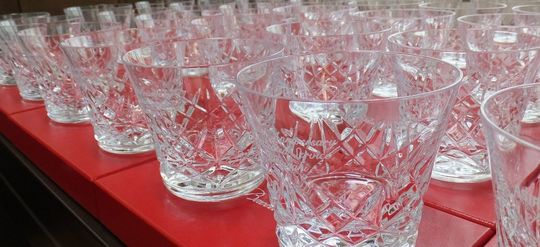 バカラのアリアタンブラー2025の大口注文の写真。レッドボックスの上に大量のグラスが整然と並べられ、側面には記念の名入れ彫刻が施されており、特別なイベントや企業への贈答品としての高級感と壮観な様子を伝えています。