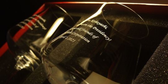 シャトーバカラワイングラスの側面に、社長就任祝いのメッセージと会社名、日付を名入れ彫刻した写真。レッドボックスの中に2客収められており、クリスタルの透明感の中に、新たな門出を祝うメッセージが美しく刻まれています。特別な贈り物としての高級感と、温かい気持ちが伝わる、洗練された逸品です。