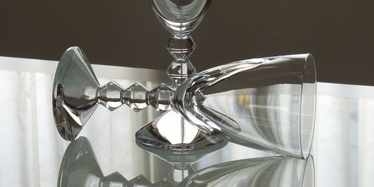 バカラワイングラスの商品紹介写真：テーブルの上に横向きに置かれたベガワイングラス。側面の美しいカットが光を反射し、バカラならではのクリスタルの輝きと洗練されたデザインが際立つレイアウトです。