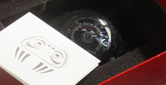 バカラのクリスタル製ダルマの底面に、格調高いエッチングで『Opening of new factory 2025』と名入れ彫刻を施したサンプル写真。透明感あふれるクリスタルの底面に刻まれたメッセージが、新工場の設立という輝かしい門出を祝し、七転び八起きの精神でさらなる発展を願う、洗練された法人向け竣工・開所記念ギフトのイメージ。