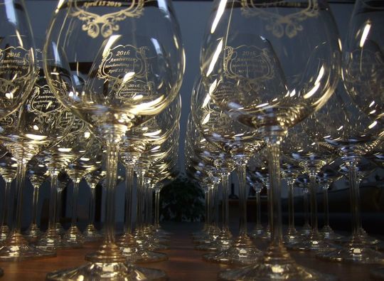 リーデルのワイングラスに20周年記念のメッセージと装飾デザインを名入れ彫刻し、50個以上がテーブルに並ぶ写真 法人向け高級記念品や周年祝いの大量注文事例