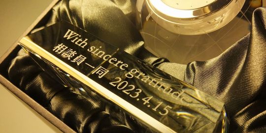 退職祝いに贈るグラスワークスナルミ 置き時計アースクロック。台座部に『With sincere gratitude 相談員一同 2023.4.15』と名入れ彫刻を施した写真