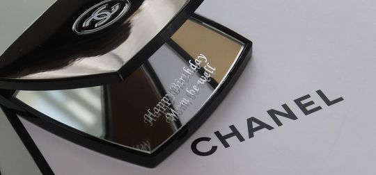 シャネルのコンパクトミラーの下のミラー中央に、『Happy Birthday Mom,be well』と名入れ彫刻を施した写真。洗練されたデザインにパーソナルなアクセントが加わり、特別な母への贈り物です。