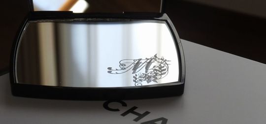 シャネルのコンパクトミラーの下部ミラーに、エレガントなバラの装飾とイニシャル『M』を名入れ彫刻した写真。華やかで繊細なデザインが高級感を醸し出す、特別なギフト仕様のイメージ。