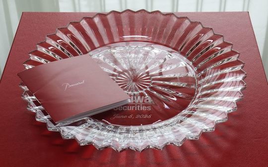 バカラのクリスタルプレート、ミルニュイ（Mille Nuits）プレートのクローズアップ写真。深いカットと繊細なエッチングが、千の夜を思わせる幻想的な輝きを放っている。プレートの表面中央に、提携する2社の企業ロゴマークが名入れ彫刻されており、周年記念品として企業間の強固なパートナーシップを象徴している。光を反射する緻密なデザインと名誉あるロゴが融合した、格式高い法人ギフト。