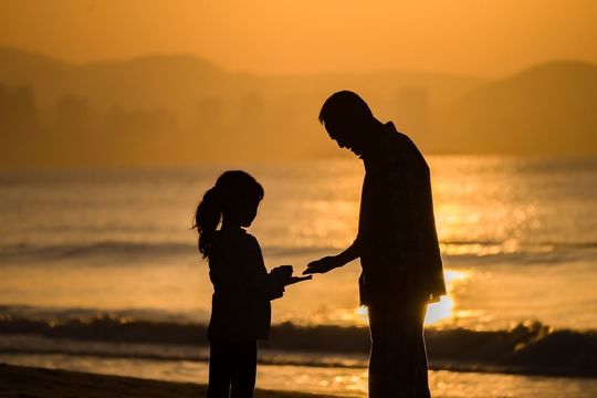 両親の誕生日に 子どもから親への贈り物 夕日が落ちる浜辺で父親と娘が貝殻を拾うシルエット写真
