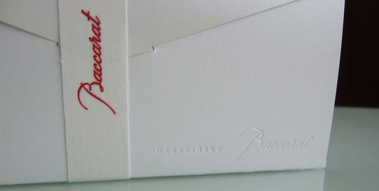 バカラの招き猫Sサイズの特別仕様ペア箱の写真。白い箱の側面に、『MANEKINEKO Baccarat』と箱にプレスされているアップ写真。エンボス加工された文字が、光の当たり方によって繊細に浮かび上がり、バカラのブランド名と招き猫のシリーズ名を上品に表現しています。