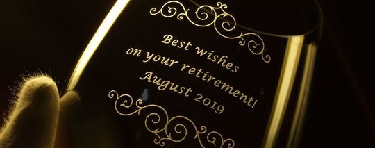 名入れ彫刻されたリーデル ワイングラス。側面に退職祝いのメッセージ“Best wishes on your retirement”と記念日入り
