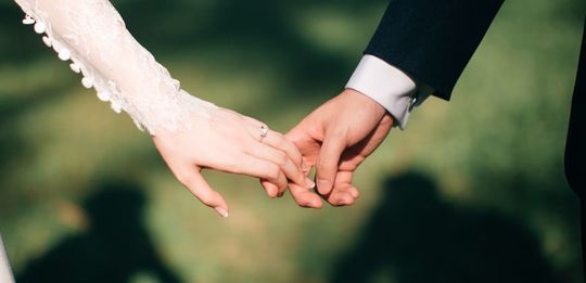 結婚式で新郎新婦が手をつなぎ、愛と絆を感じさせる手の拡大写真。新たな人生を共に歩む二人の誓いが感じられる、温かく心に残る瞬間