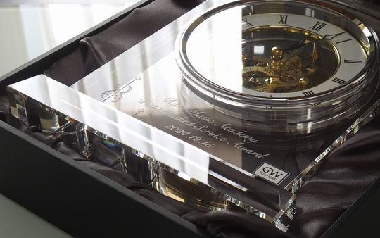 グラスワークスナルミのマルカートスケルトンクロック。透明なムーブメントの下に、音楽学校の名前、Award名、日付の3行が名入れ彫刻されています。文字の左側には、学校のロゴであるバイオリンのデザインも精巧に彫り込まれた、特別な記念品や表彰の贈り物に最適な写真です。