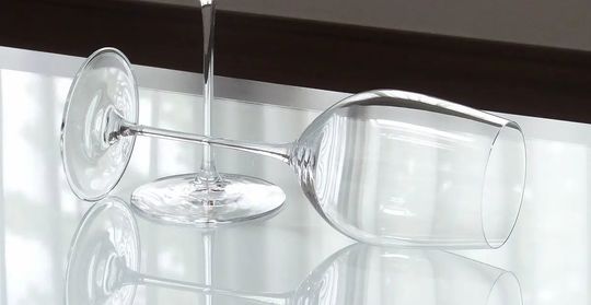 ティファニー商品一覧ページ: テーブルの上に、エレガントに立つティファニー ホームエッセンシャル ワイングラスと、その隣に優雅に横たわるグラス。洗練されたデザインと輝きが際立ち、ギフトとしても最適です。