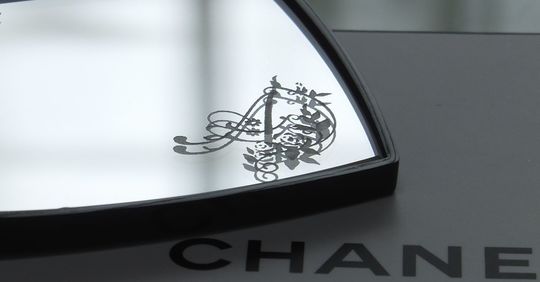 シャネルのコンパクトミラーの下部ミラーに、エレガントなバラの装飾とイニシャル『A』を名入れ彫刻した写真。華やかで繊細なデザインが高級感を醸し出す、特別なギフト仕様のイメージ。