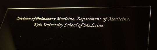 グラスワークスナルミのフォトフレームに慶応大学医学部の記念品としてメッセージを名入れ彫刻した写真。特別な記念日や功績を讃えるために施されたオーダーメイドの彫刻が、贈る人と受け取る人の絆を深める