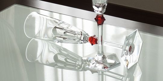 バカラグラスの商品紹介写真：テーブルの上に横向きに置かれたアルクールイブシャンパングラス。側面の美しいカットが光を反射し、バカラならではのクリスタルの輝きと洗練されたデザインが際立つレイアウトです。