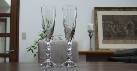 バカラのシャンパングラス、ベガシャンパングラスがリビングダイニングテーブルの上に置いてある写真。ペアグラスとして並べられたベガシャンパングラスは、そのユニークなステムと光を反射するクリスタルの輝きで、リビングダイニング空間に洗練された華やかさを添え、特別なひとときを演出しています。