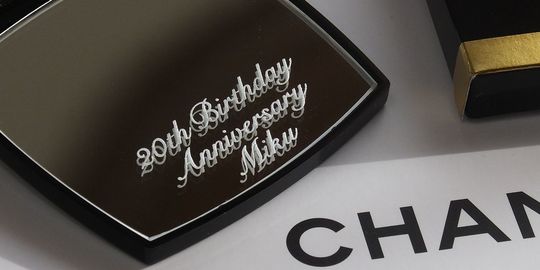 20歳の誕生日祝いに最適な、シャネルのコンパクトミラーに『20th Birthday Anniversary Miku』と名入れ彫刻を施したアップ写真。特別な節目を祝う、パーソナルで心温まるギフトの細部が際立っています。