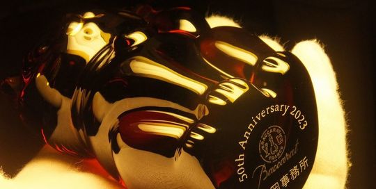 バカラの招き猫 レッドの底面に、『50th Anniversary 〇〇事務所』と名入れ彫刻した写真。情熱的な赤いクリスタル製の招き猫の底に、50周年を祝うメッセージと事務所名が繊細に刻まれています。企業の節目を祝う特別な贈り物として洗練された逸品です。