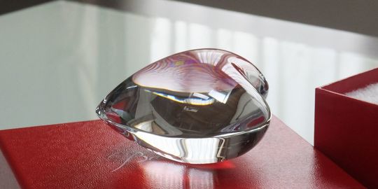 バカラオブジェの商品紹介写真：ハートペーパーウェイトが、バカラの象徴である赤いギフトボックスの上に美しく置かれている写真。贈り物としての高級感と、愛らしいデザインが際立つレイアウトです。