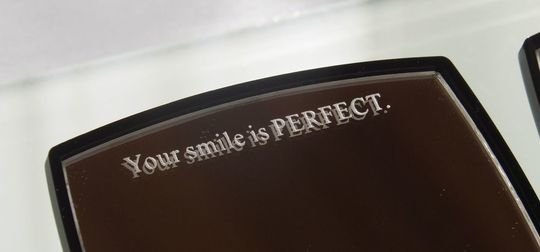 シャネルのミラー上部に、『Your smile is Perfect』と名入れ彫刻が施された写真。自分だけの特別感を演出する、繊細でエレガントなパーソナルギフトのイメージ。