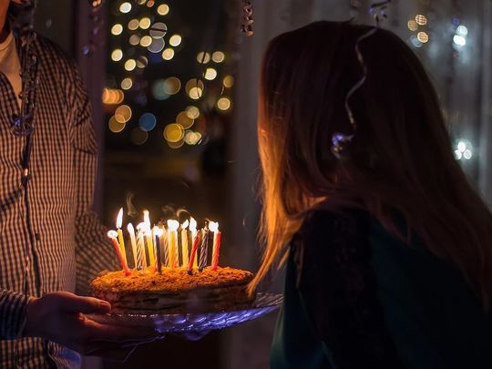 暗がりの中、ホールケーキにたくさんのろうそくが立てられ火が灯っている。これを女性が吹き消そうとしている写真。誕生日パーティーの一幕を捉えた、温かくお祝いムードに包まれた瞬間です。