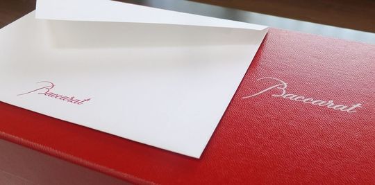 バカラのレッドボックスの上に、バカラのメッセージカードが置かれている写真。贈り物としての高級感と、バカラの象徴的なパッケージが、特別なメッセージを添えることで、よりパーソナルで心温まる印象を与えています。