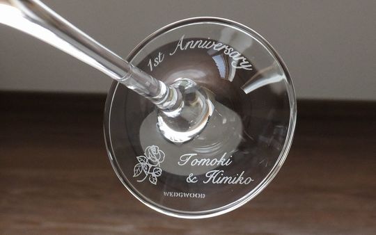 ウェッジウッド プロミシス ウィズ ディス リング シャンパングラスの底面に「1st Anniversary」、二人の名前、そして優雅なバラのデザインが名入れ彫刻された写真