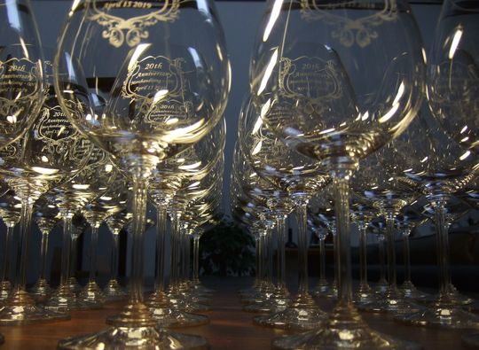 リーデルのワイングラスが並んだ写真。側面に20周年記念のメッセージと歴史的な装飾デザインが加わり、贈り物としての価値を高めています