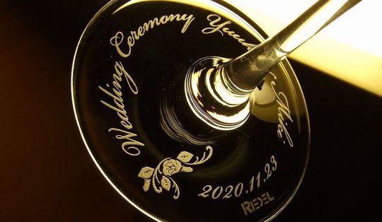 リーデルのワイングラスの底面に「Wedding ceremony」の文字とお二人の名前、記念日を名入れ彫刻し、華やかなワンポイントのフラワーデザインを添えた特別な結婚祝いのギフト。美しいデザインが、結婚式の思い出をより一層華やかに彩ります
