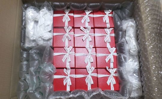 バカラグラスを安全かつ確実に配送するため、40個以上のグラスが緩衝材（プチプチや紙）を隙間なく敷き詰めた大きな段ボール箱に整然と梱包されている写真。高額なクリスタル製品の輸送中の破損を厳重に防ぐためのプロフェッショナルな梱包技術と、大量注文への対応力を伝える情景。