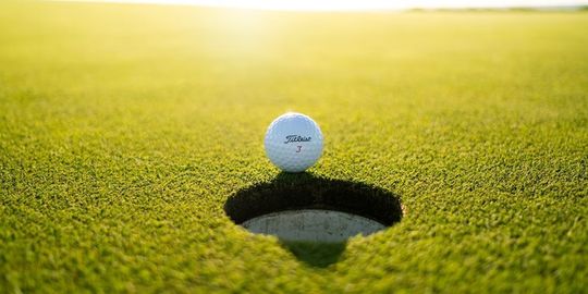 ゴルフグリーンのカップの近くにゴルフボールがある写真