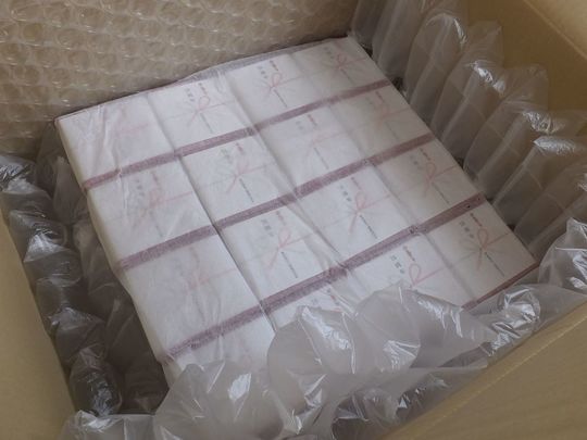 包装紙と熨斗で丁寧に包まれたバカラのレッドボックス16個が段ボールに梱包され、印刷保護用の紙が熨斗の上に載せられている写真 高級ギフトの丁寧な包装・発送対応事例