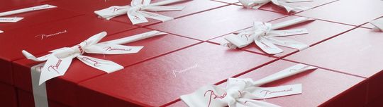 バカラのペアグラスが入るサイズのレッドボックスにリボンが結ばれた箱が、たくさん美しく並べられている写真。ギフトとしての豪華さと、バカラの象徴的なパッケージが持つ特別感を強調しています。