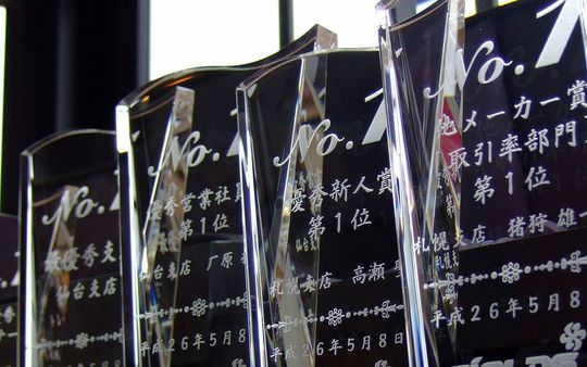 社員表彰に贈るクリスタルトロフィー4点並び写真 『No.1』のタイトルと優秀営業社員賞、優秀新人賞、最優秀支店、受賞者名、日付、企業ロゴを名入れ彫刻