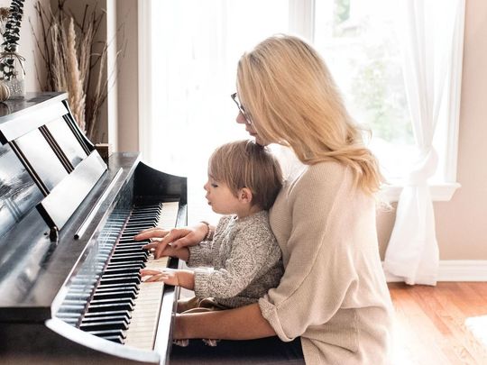 母の膝の上に3歳くらいの子供が乗り、一緒にピアノを弾いている写真。親子の温かい絆と、音楽を楽しむ微笑ましい瞬間が捉えられています。