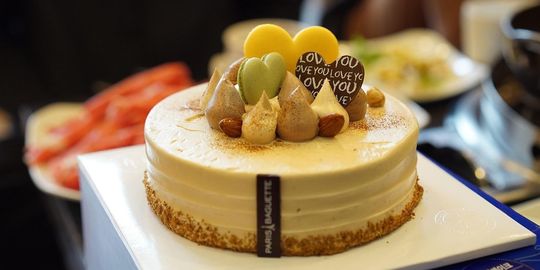 誕生日のお祝いのホールケーキ。ケーキの上には、ハート型のマカロンとハート型のチョコレートが可愛らしく飾られており、甘くて華やかなお祝いの雰囲気を演出しています。