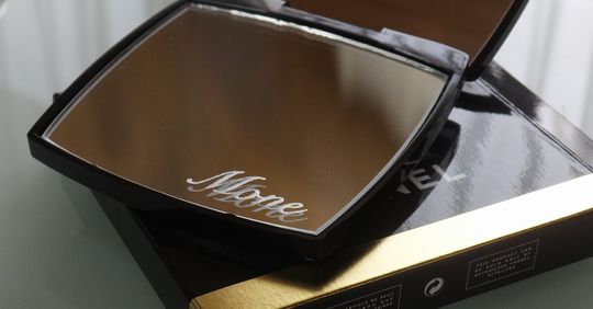 シャネルのギフトボックスの上に置かれた、下部ミラーに『Mone』の名入れ彫刻があるコンパクトミラー。ブランドの高級感とパーソナライズされた特別感が伝わる写真。