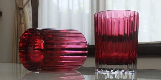 バカラグラスのハーモニータンブラー レッドが2客、テーブルの上に置いてある写真。縦に施された繊細なカットが特徴の赤いタンブラーが2つ並び、クリスタルの美しい輝きが、ペアグラスとしての特別感と、特別な日を彩るテーブルウェアとしての魅力を際立たせています。