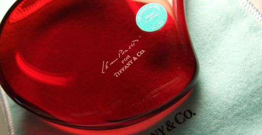 ティファニー商品一覧ページ: テーブルの上に置かれたティファニークリスタルハートペーパーウェイト（レッド）のアップ写真。鮮やかな赤色が目を引き、ギフトや記念品に最適な美しいクリスタル製品です。