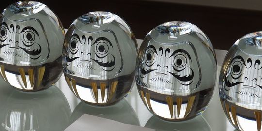 バカラオブジェの商品紹介写真：テーブルの上に横一列に並べられた、バカラのダルマ4点のアップ写真。それぞれのダルマが持つ表情と、クリスタルの輝きが際立つレイアウトです。