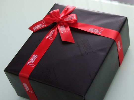 リーデルのブランドボックスがリーデル専用の包装紙で包まれ、ブランドロゴ入りリボンが丁寧に結ばれた高級感あるギフト包装の写真 贈答用・記念品にふさわしい上品なラッピング事例